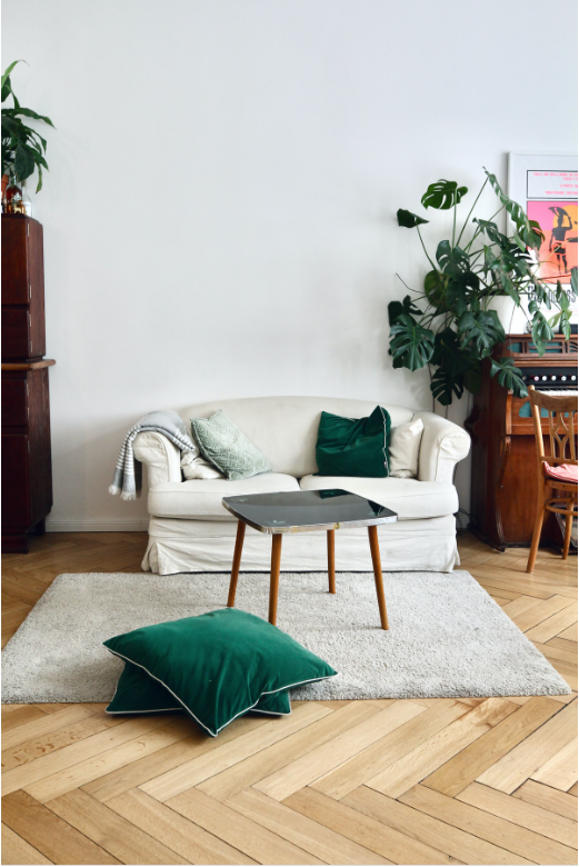 Herringbone natural Scandinavian hardwood, blonde wood flooring, plush pile off-white area rug, green throw pillows, white plush sectional 